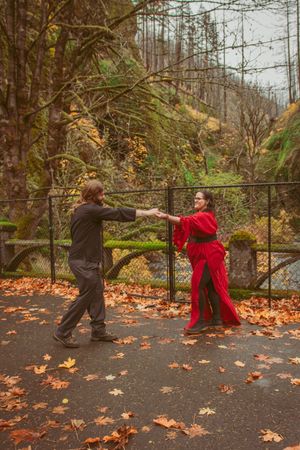 A couple enjoying playful moments on a leaf-covered path near a railing during autumn.
