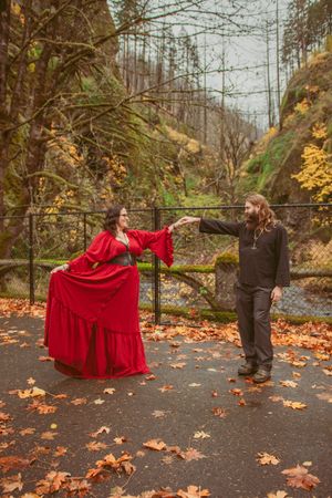 A couple in contrasting red and black outfits striking a dramatic dance pose among fallen leaves.