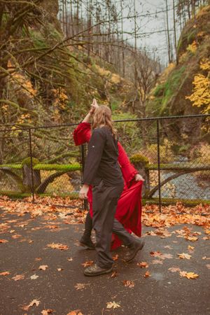 Two figures dancing outdoors in autumn with fallen leaves, one wearing a flowing red dress and one in darker clothing.