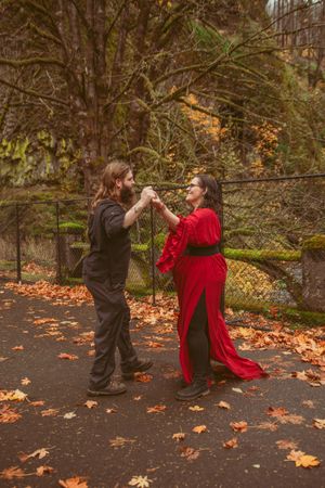 A couple performs dramatic dance moves among autumn leaves on a forest path in fall.