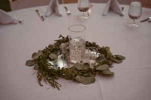 Wedding table centerpiece featuring a glass candle holder surrounded by a lush green wreath.