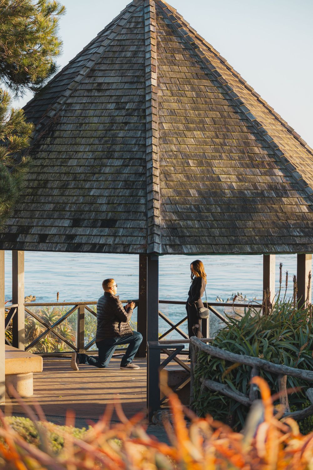 Romantic proposal scene in a gazebo overlooking the ocean at sunset.