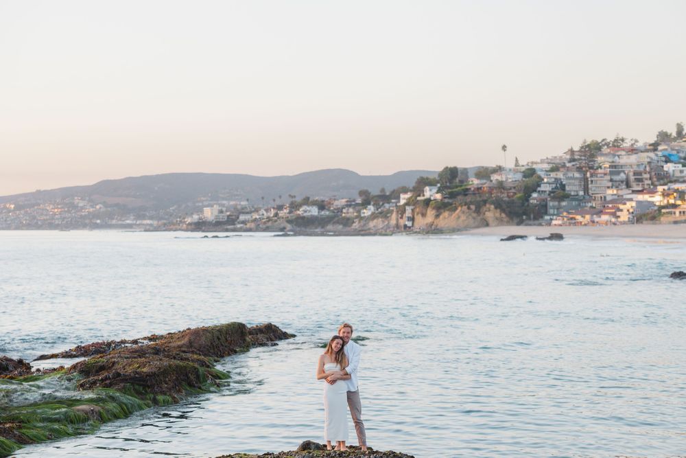 Couple embraces on rocky coastal outcrop during sunset.