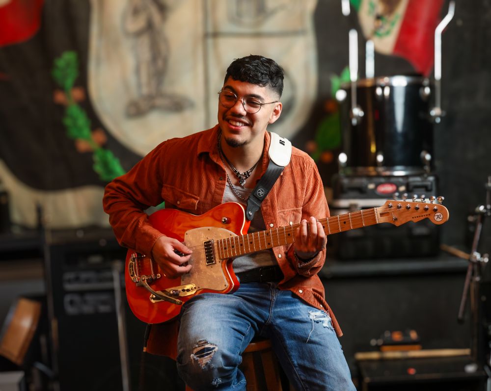 Musician performing with orange guitar on stage with dramatic lighting.