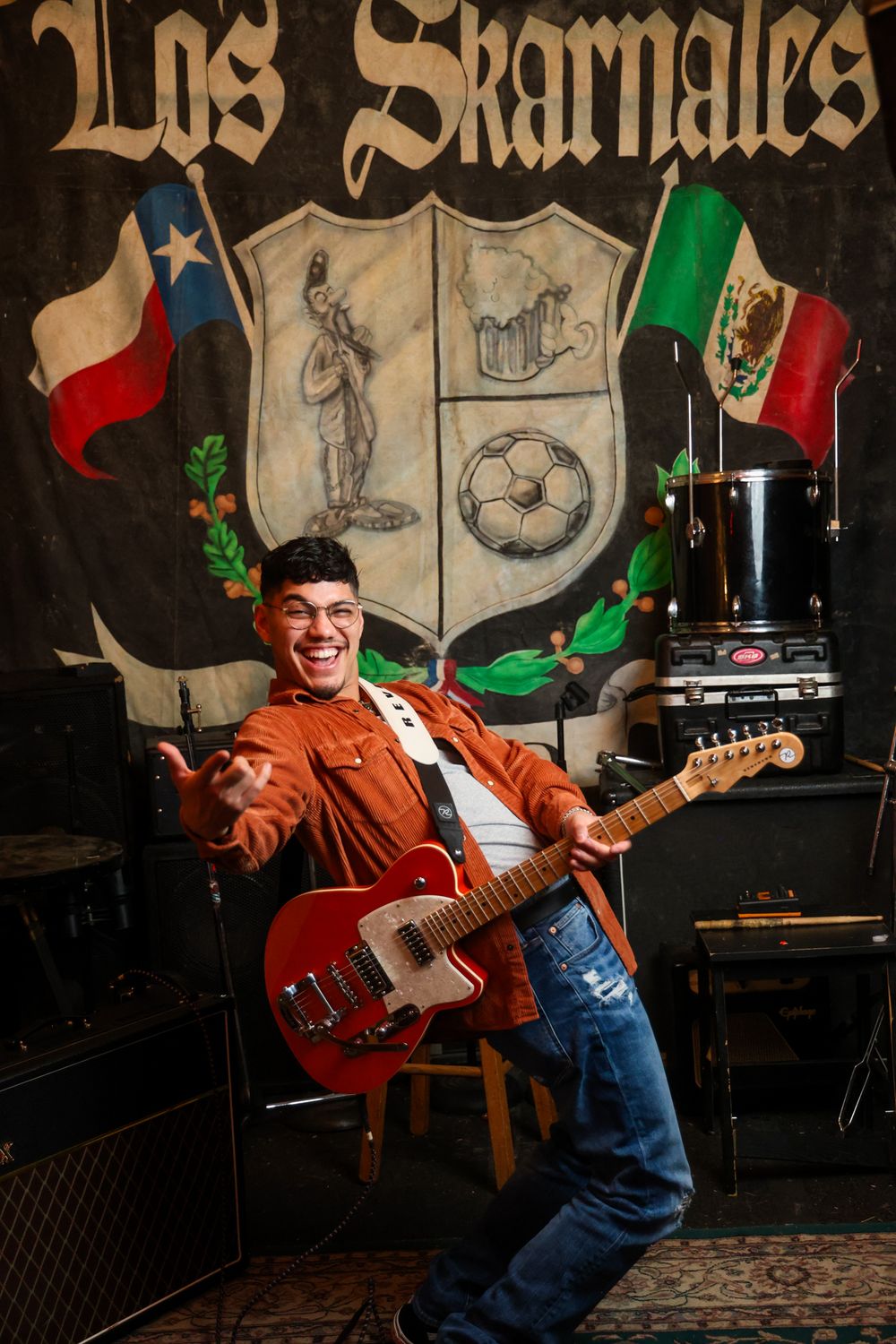 Musician plays guitar with animated expression in front of decorated stage backdrop.