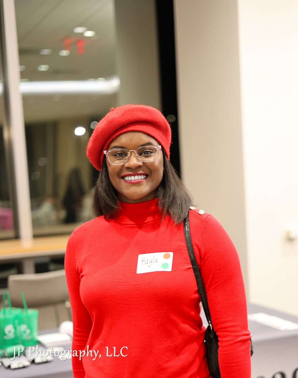 Professional event attendee wearing a bright red turtleneck and beret with glasses at an indoor gathering.
