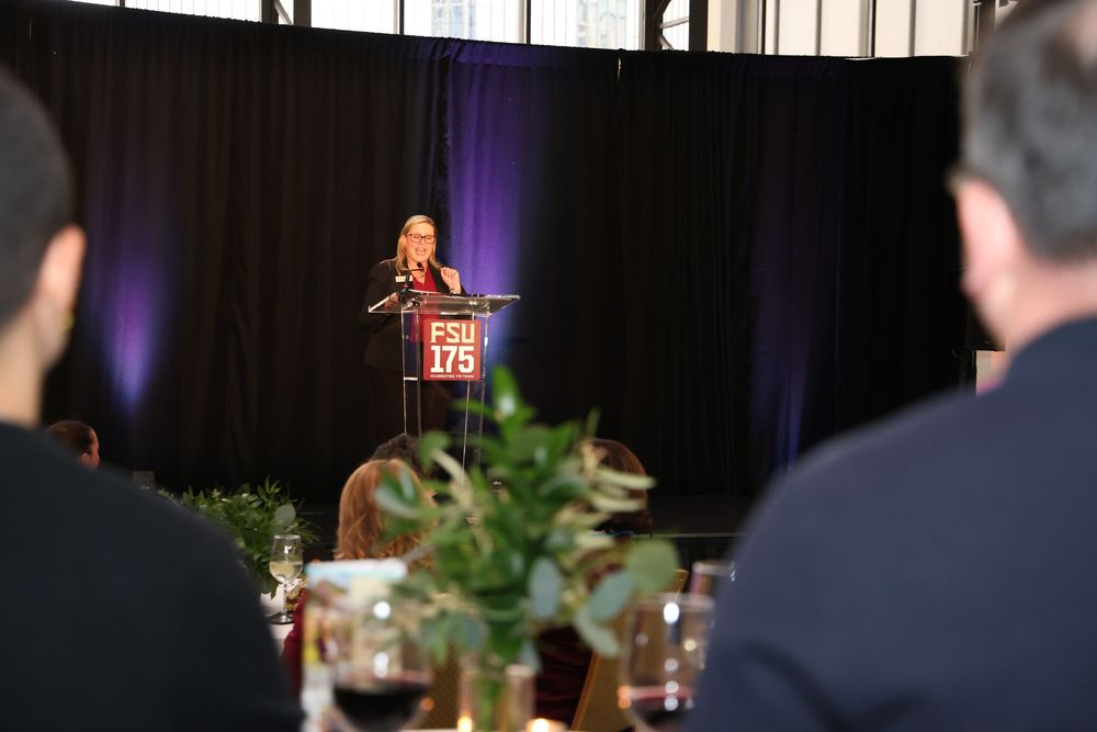 Speaker at FSU 175th anniversary podium addresses audience at formal banquet event with purple lighting.
