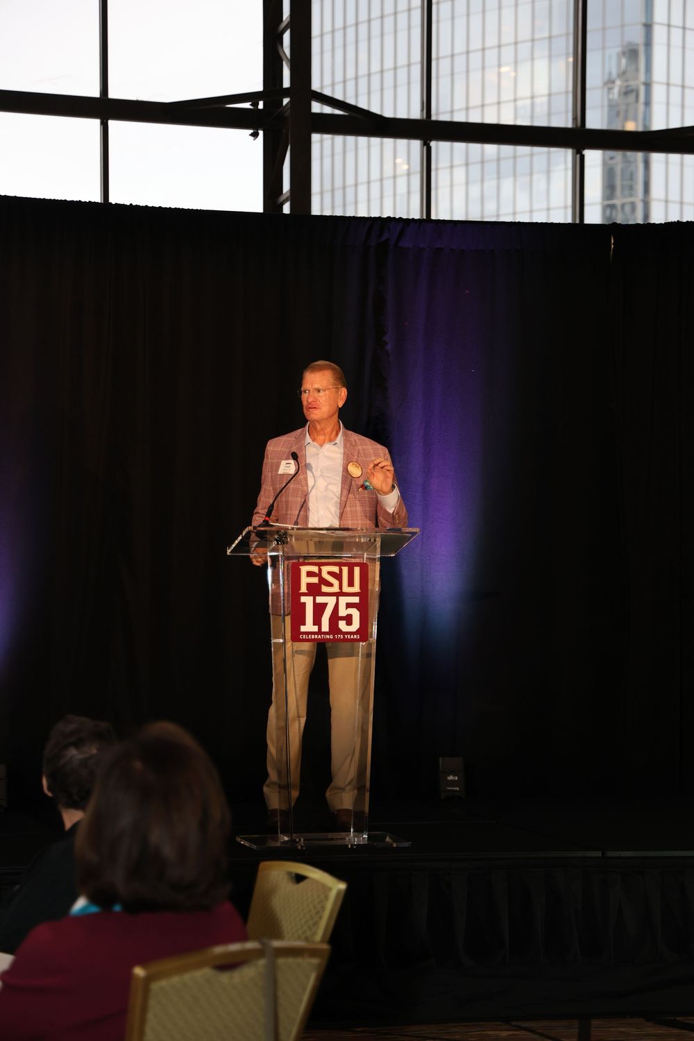 A speaker presents at a podium during FSU's 175th anniversary celebration event in a conference hall.