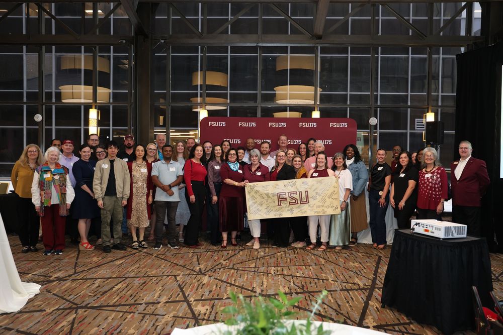 Large group of FSU alumni posing together indoors holding an FSU banner at a university gathering event.