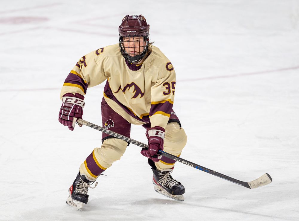 Hockey player in cream colored jersey positions for play during ice hockey match.