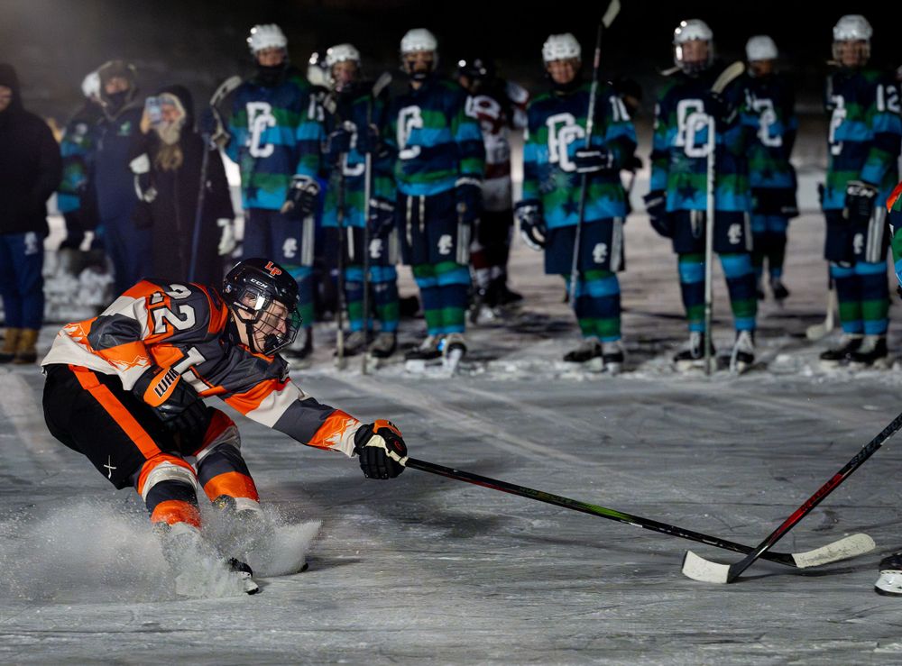 Hockey player in orange jersey glides across ice with stick and puck.