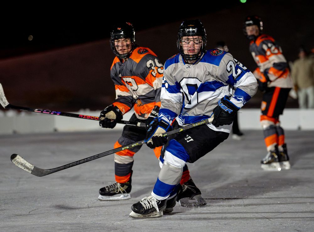 Two hockey players battle for position on the ice during an intense game between blue and orange teams.