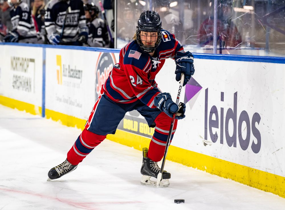 Ice hockey player in red jersey handles puck along boards near Leidos advertisement.