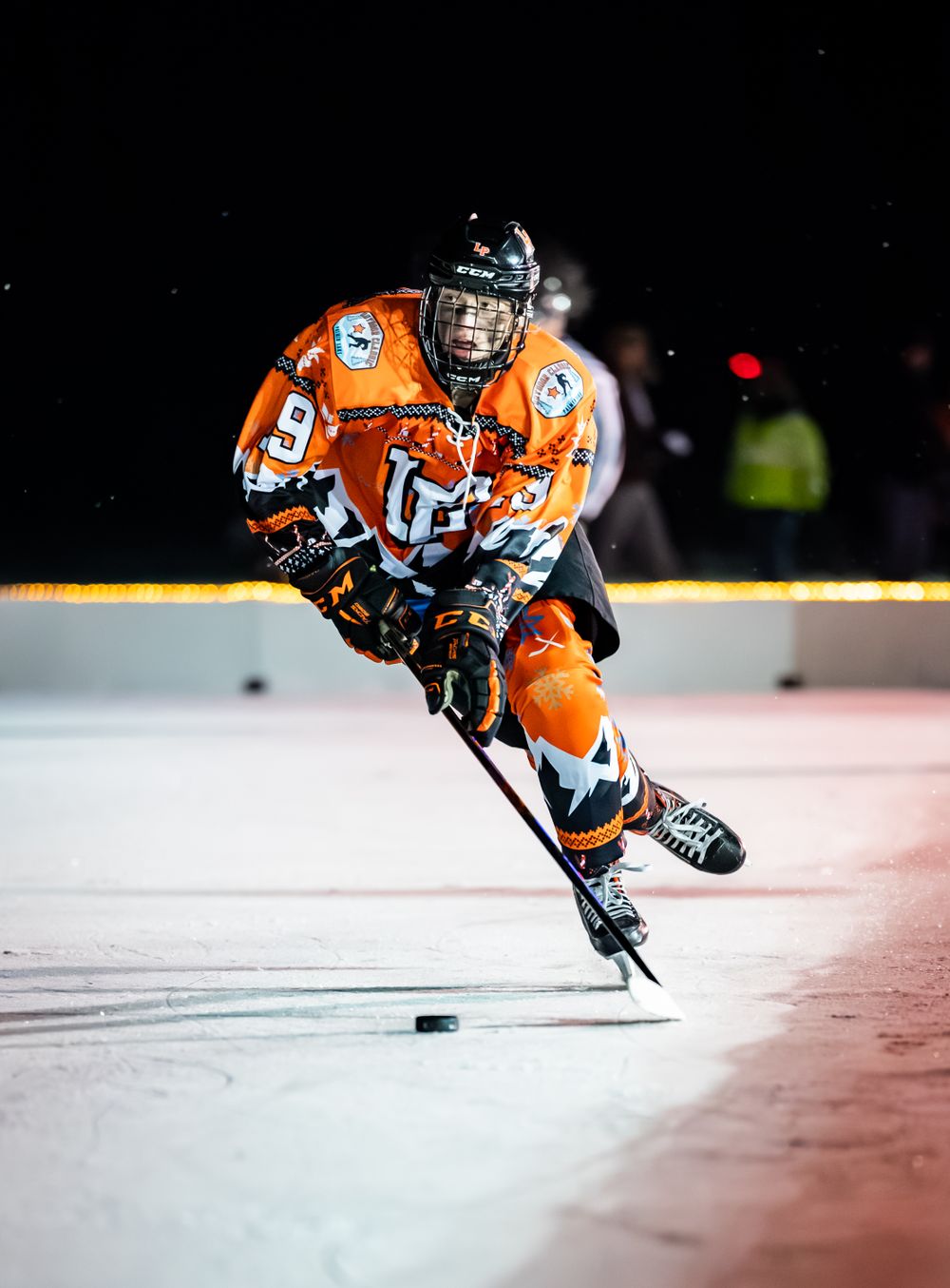 Hockey player in orange jersey controls puck on ice during intense game action.