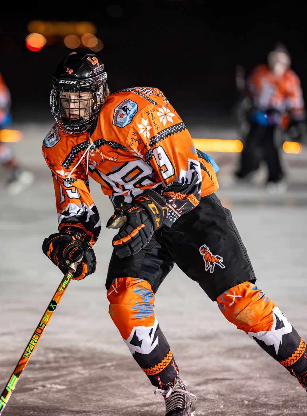 Ice hockey player in vibrant orange uniform maneuvers with stick during nighttime game.