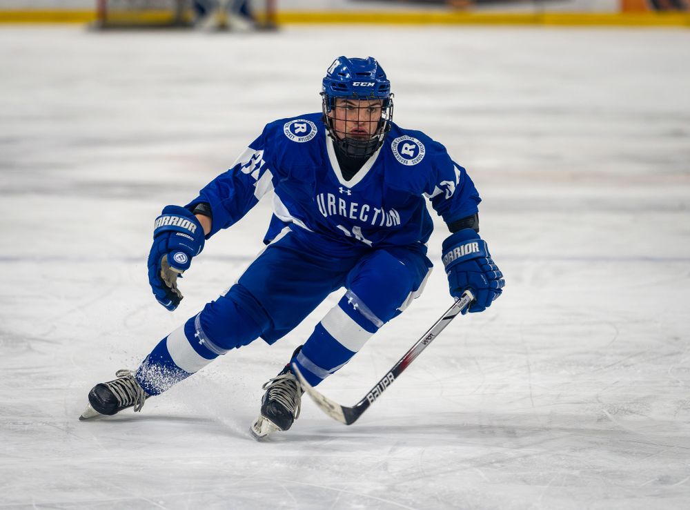 Hockey player in blue jersey performs tight turn on ice during game.