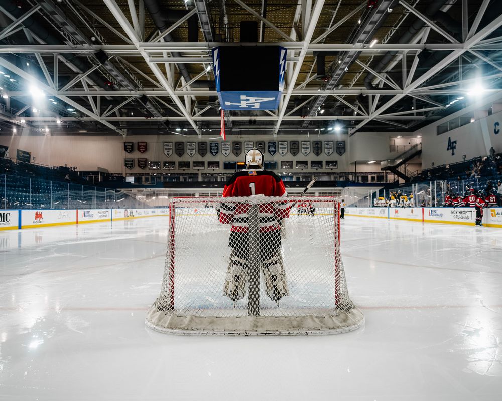 Hockey goalie stands ready in net during game with arena lights overhead.