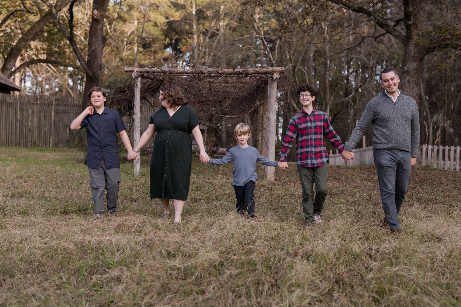 A family holds hands while walking together through a grassy field on an autumn day.