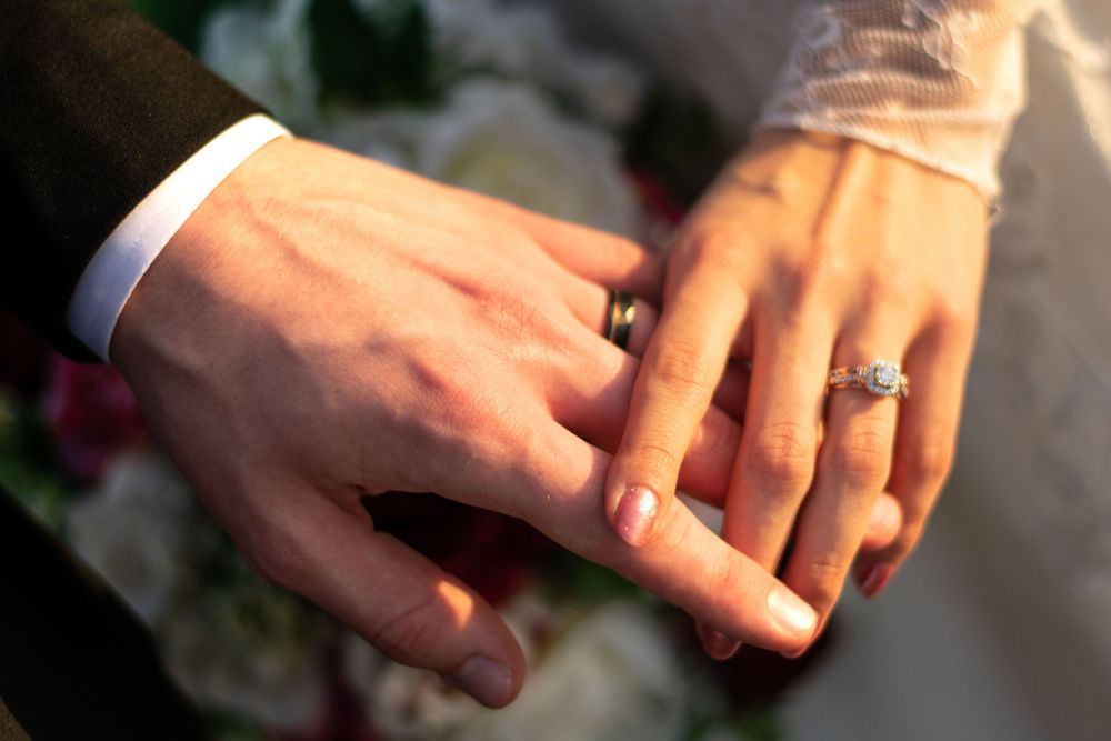 Husband and Wife holding their rings togther.