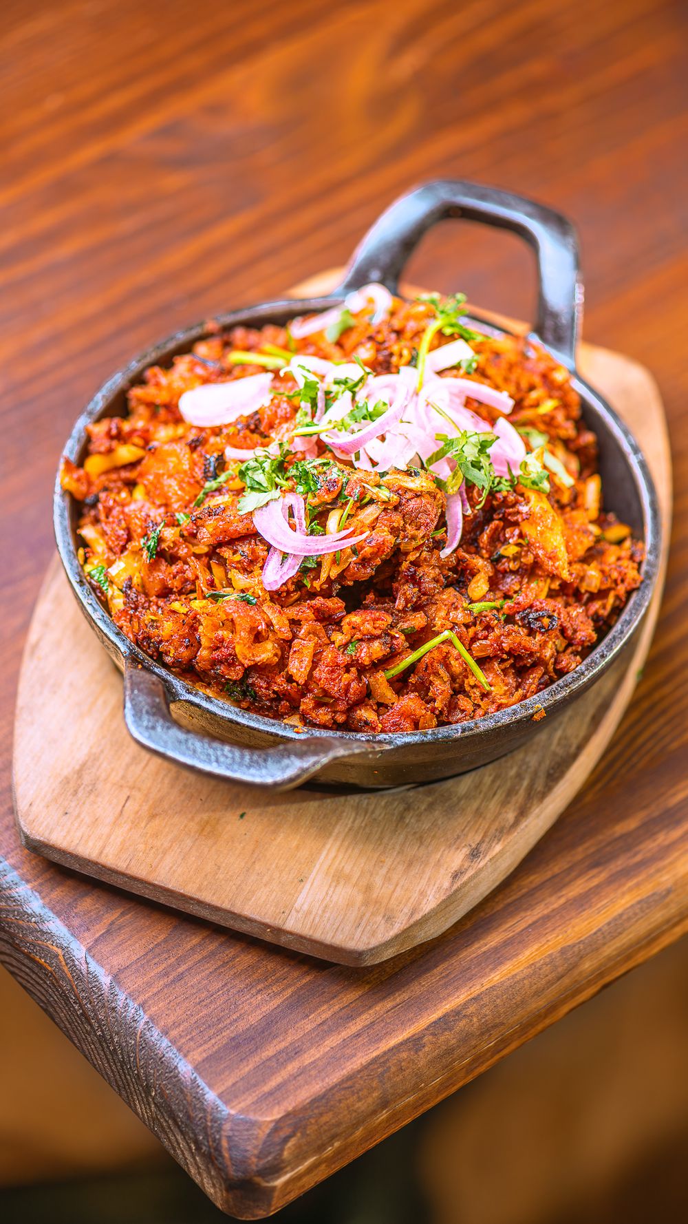Spicy Indian keema dish served in a cast iron skillet on a wooden board, topped with fresh sliced onions and herbs.