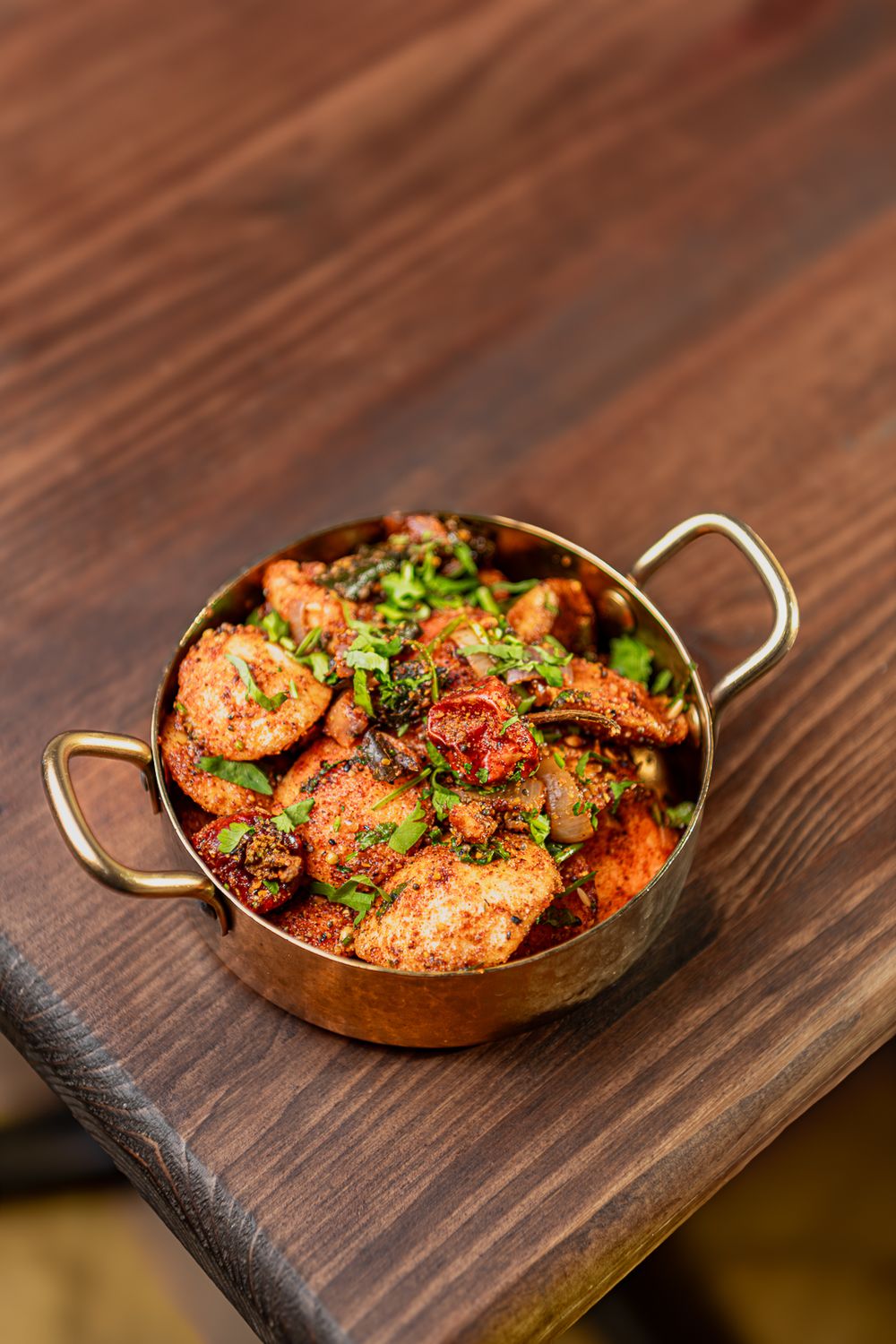 Spicy Indian chicken curry served in a traditional copper karahi bowl on a rustic wooden table.