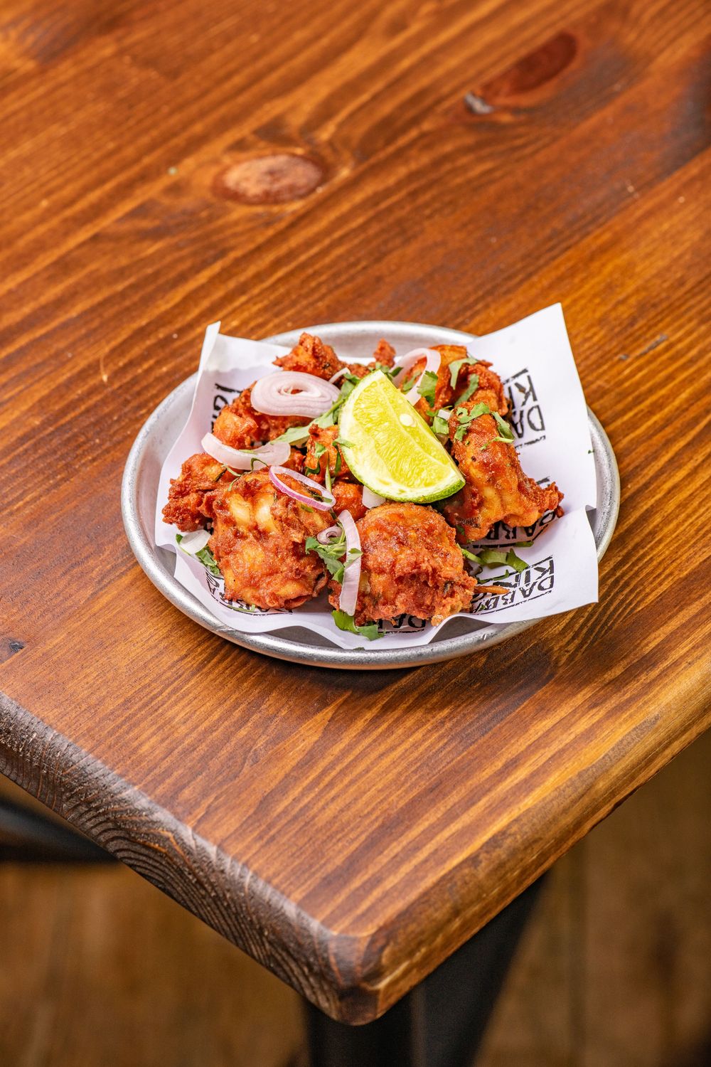 Crispy fried chicken pieces garnished with lime wedge and pickled onions served on a plate atop a wooden table.