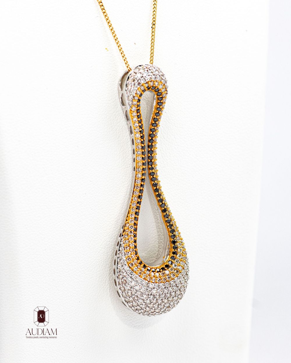 Gold and diamond pendant necklace featuring a curved teardrop design on white background.