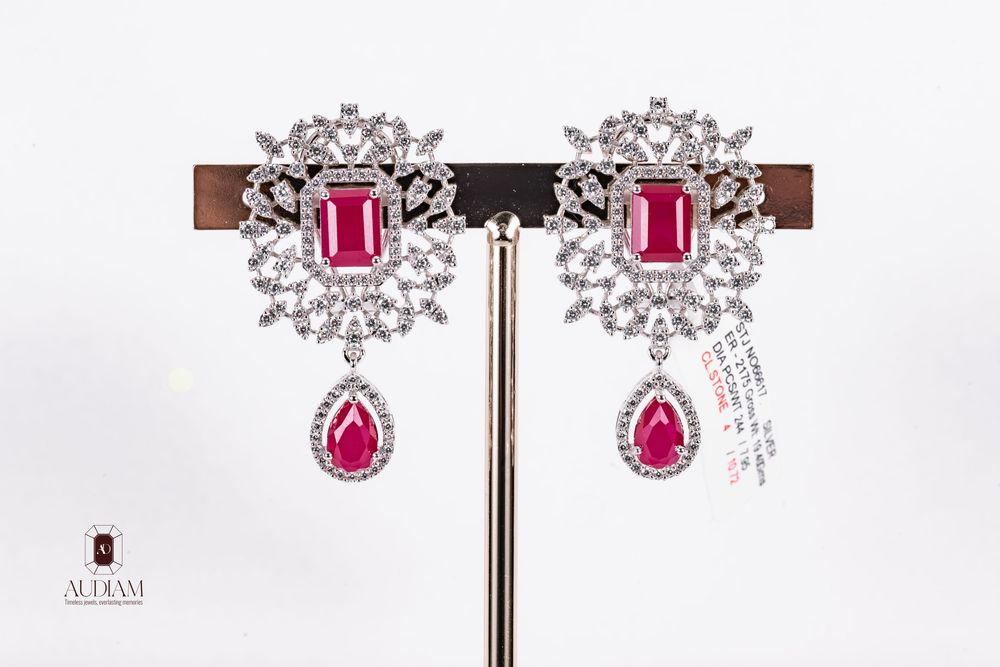 Sparkling silver-toned earrings with pink gemstones and crystal accents displayed on dark wooden stand.