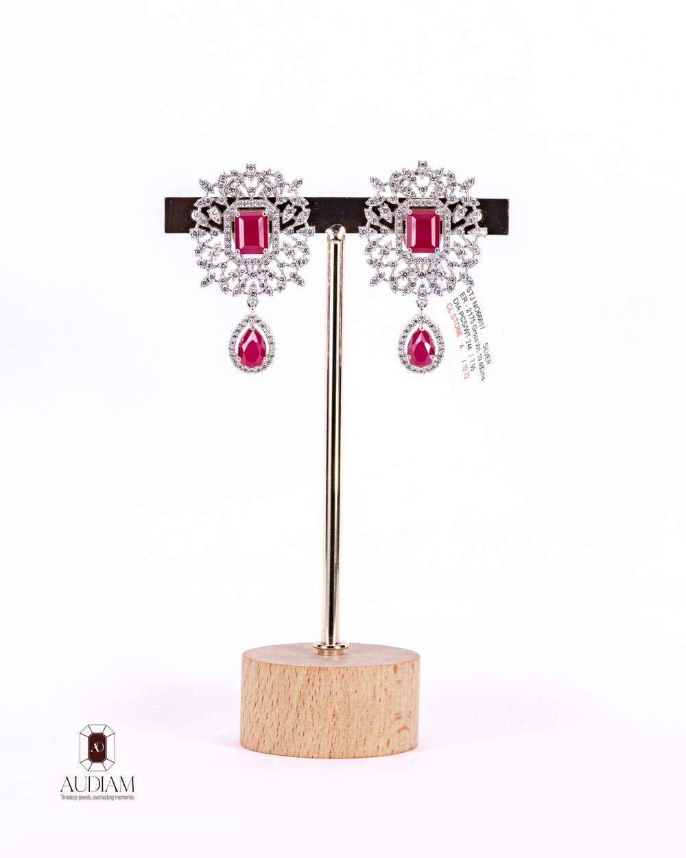 Sparkling ruby and diamond earrings with floral cluster design displayed on wooden stand.