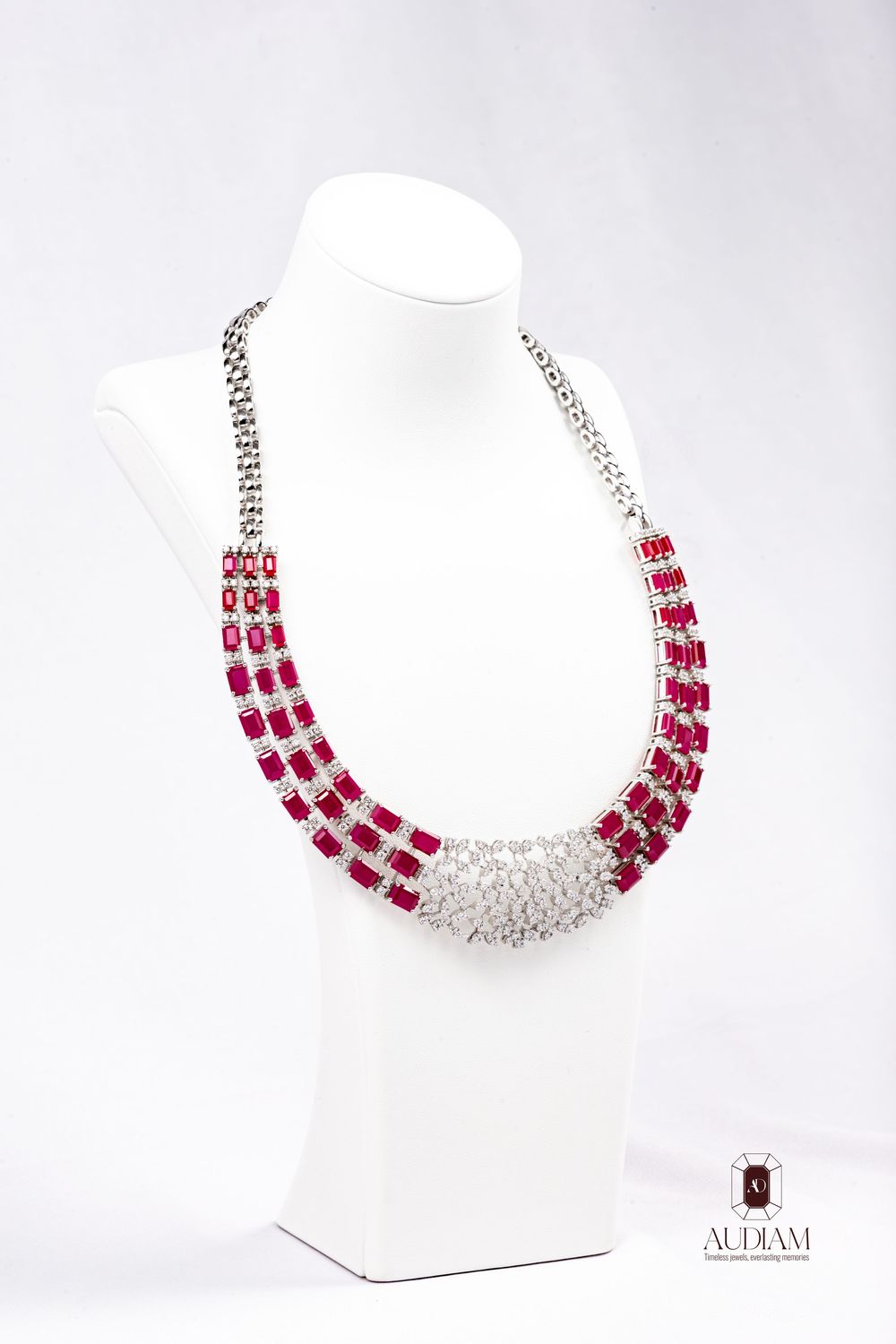 Elegant ruby and diamond statement necklace featuring three strands of deep red gems with crystal accents on white display.