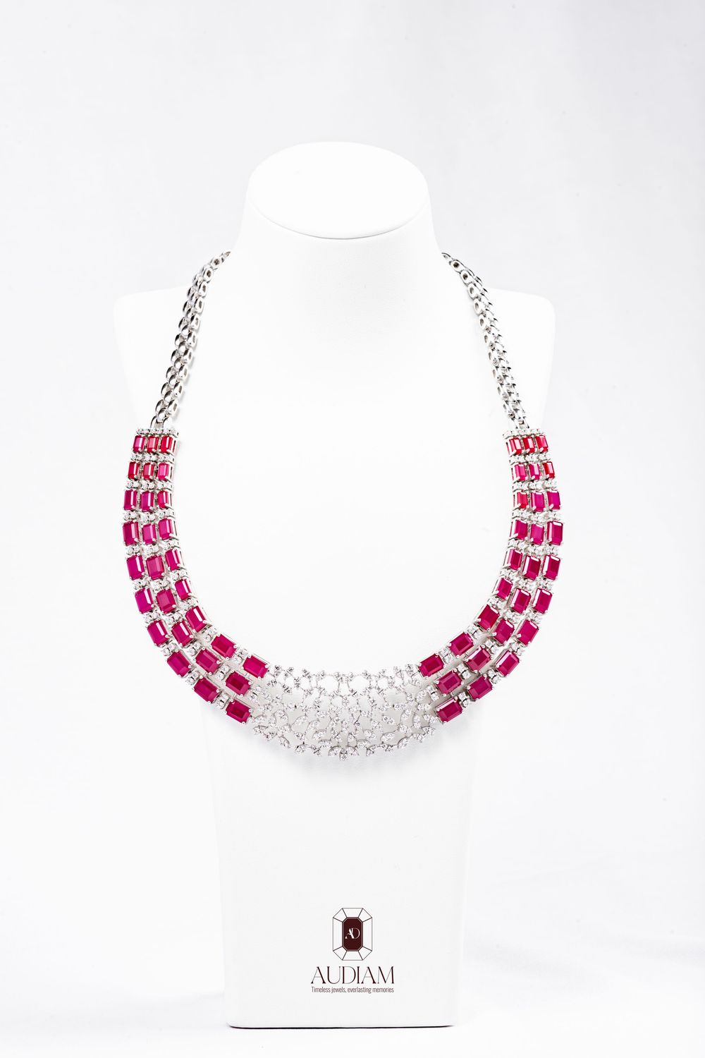 Elegant pink and clear crystal statement necklace with three rows of stones in silver-toned setting against white backdrop.