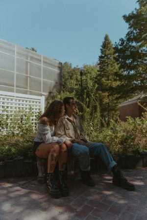 A couple are sitting beside each other on a bench outside.