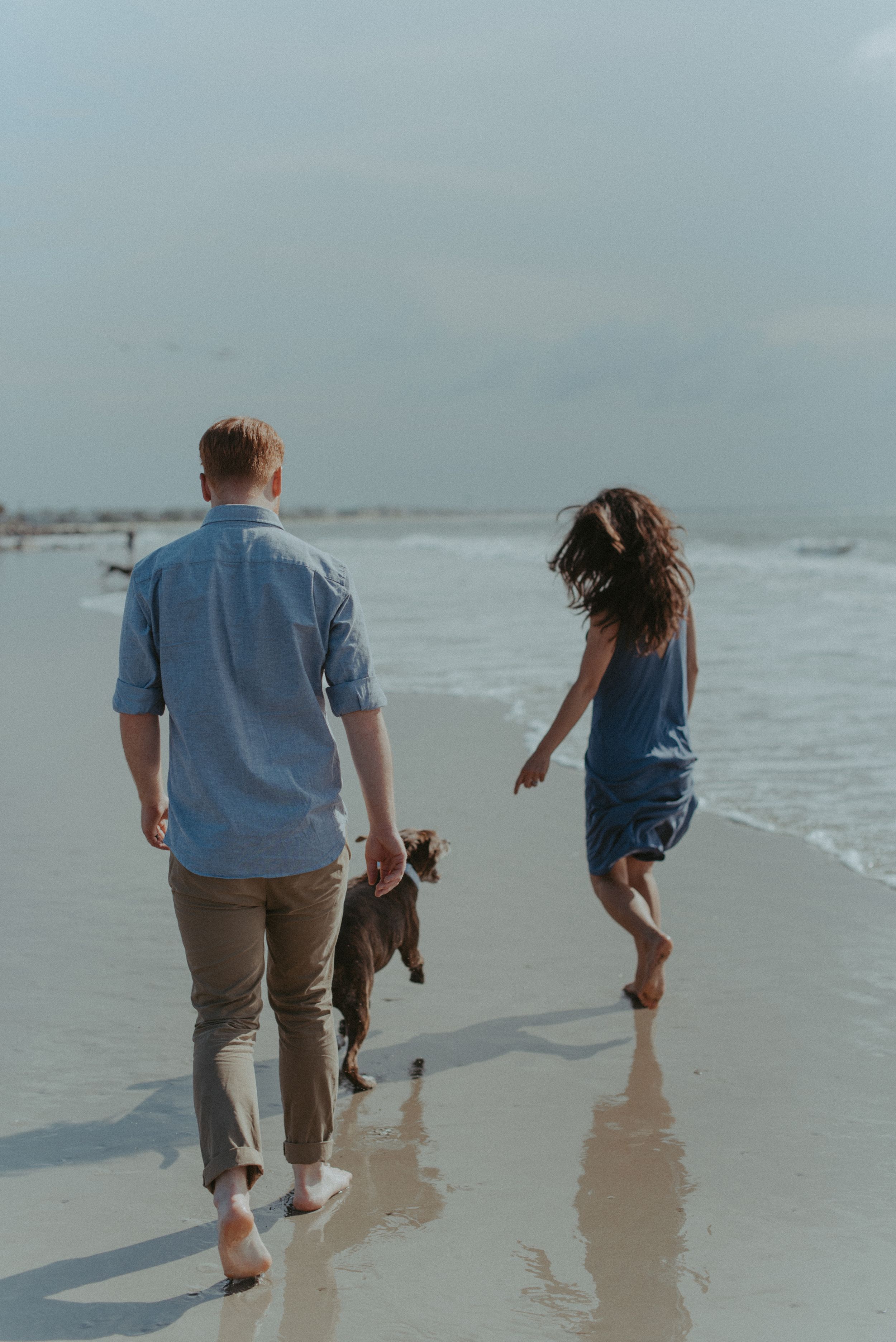 A portrait of a couple running on the beach together with their dog.