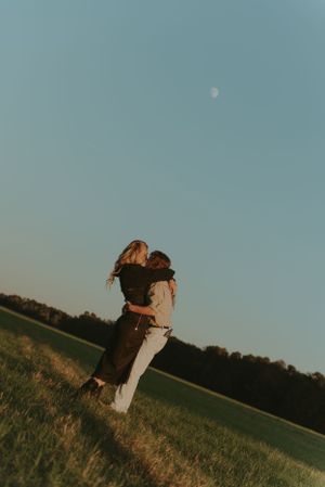 A couple are embracing each other in an open field.