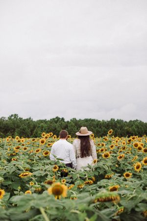 A couple standing together in a sunflower field not facing the camera.