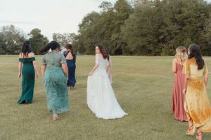 A bride is walking and smiling in a field surrounded by her bridesmaids.
