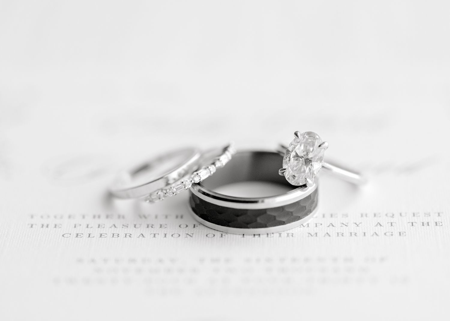 Wedding rings including diamond engagement ring and bands arranged on textured white surface.