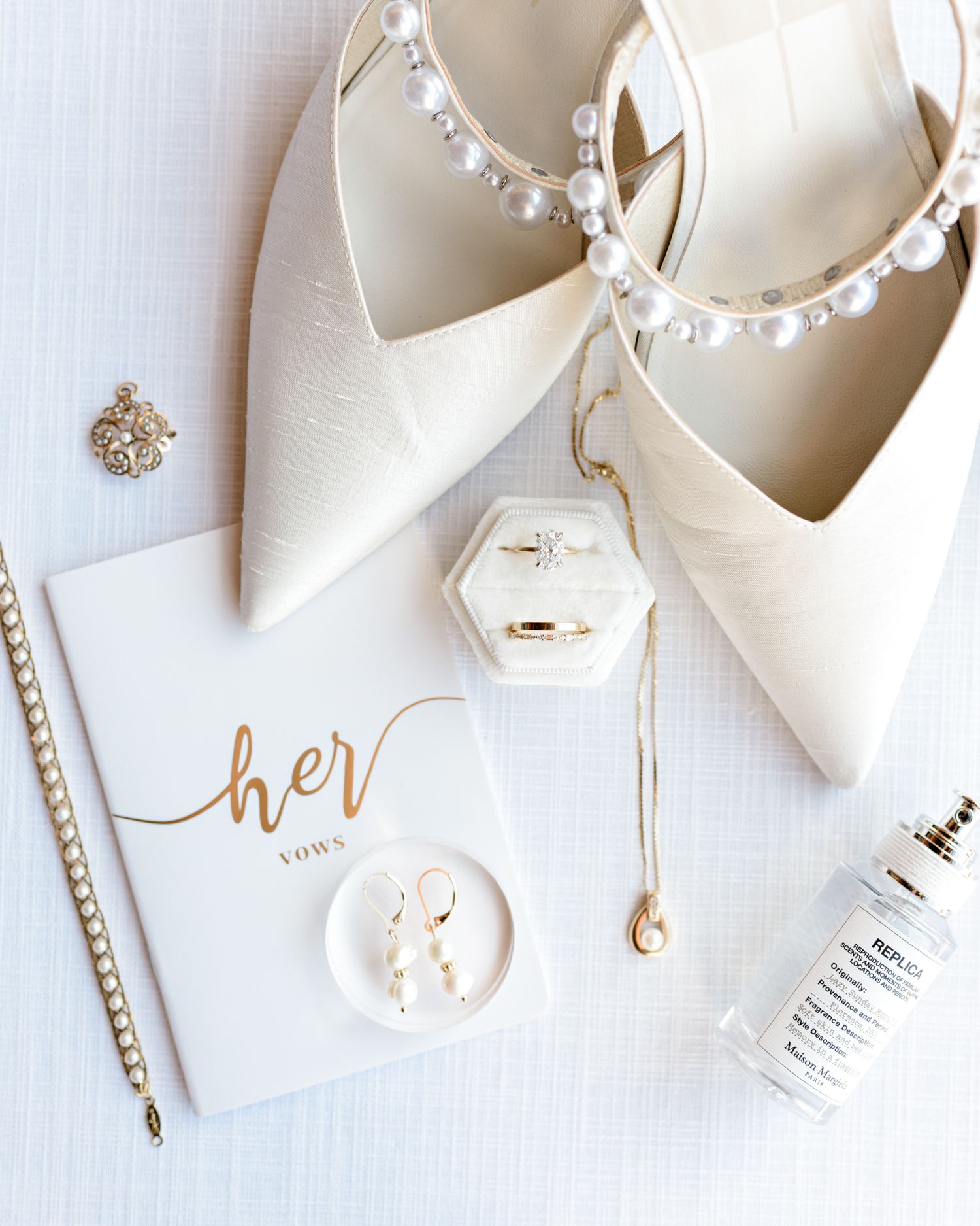 Bridal accessories flatlay with pearl-adorned shoes, jewelry box and wedding day details in white.