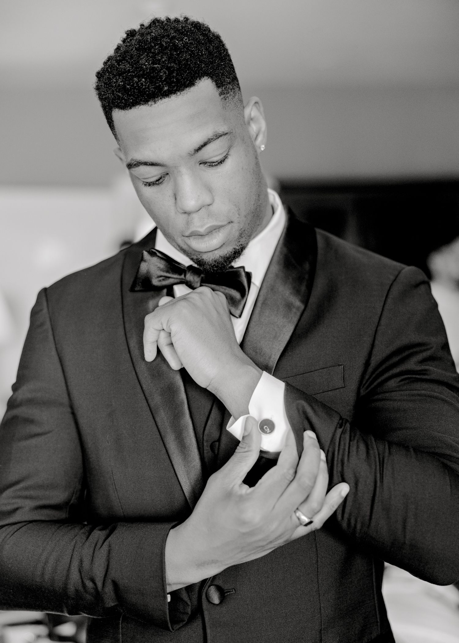 A formal black and white portrait of someone adjusting their bowtie and cufflinks.