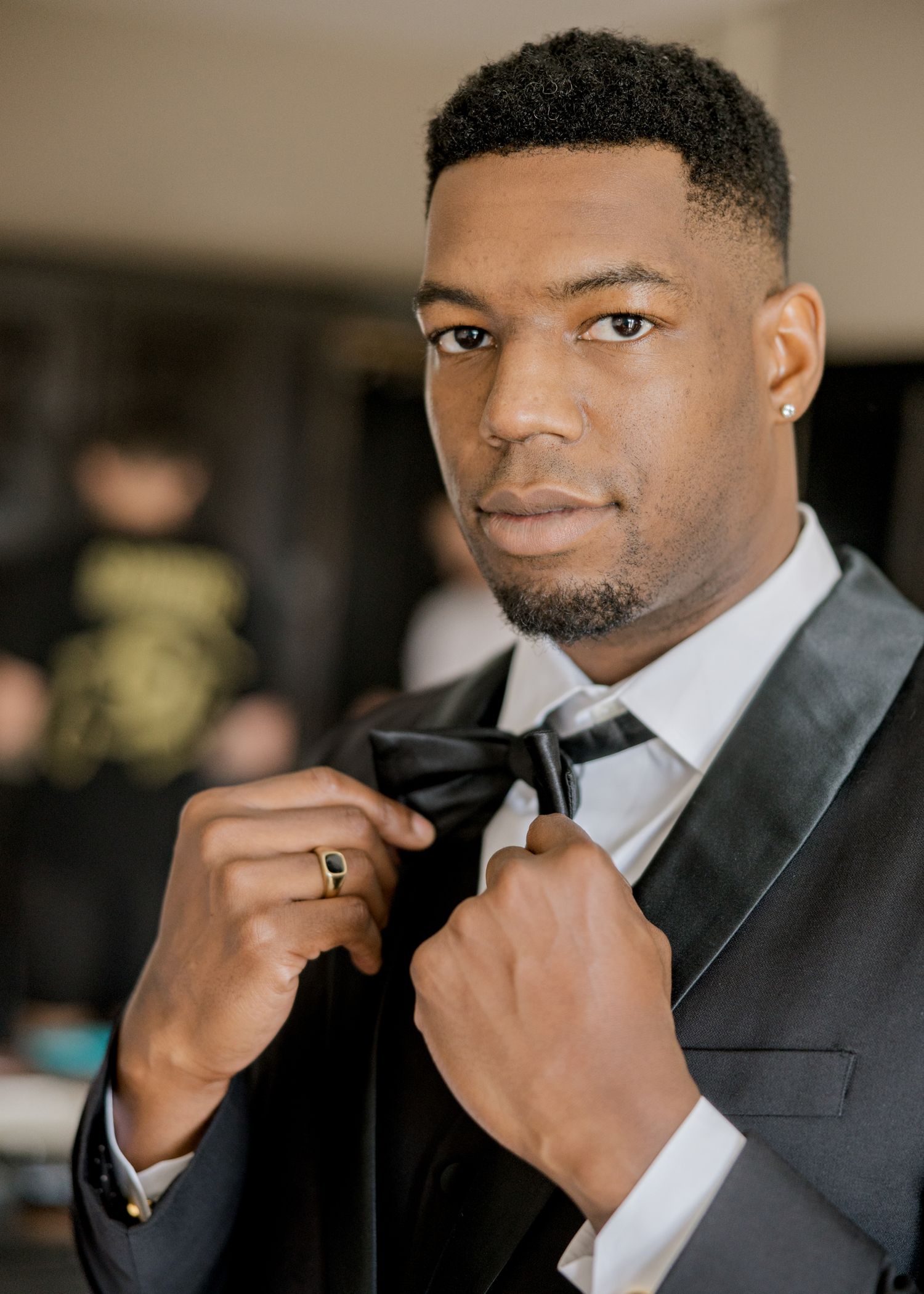 A formal portrait showing someone adjusting their bowtie while wearing a classic tuxedo.