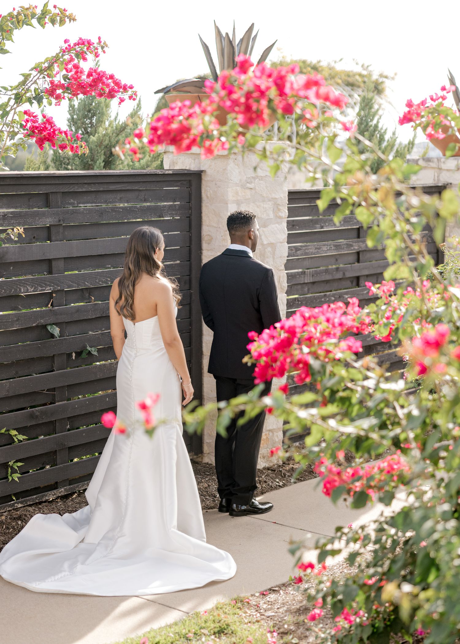 A couple shares their first look moment in a garden path surrounded by vibrant pink bougainvillea flowers.