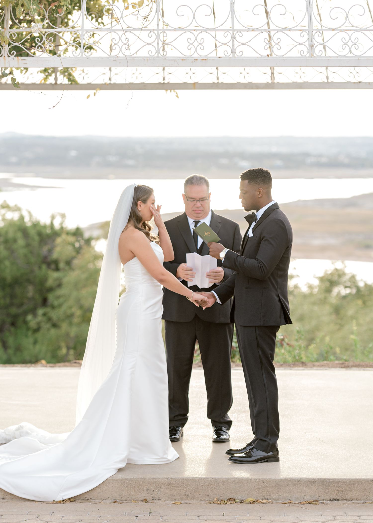 Wedding ceremony under an ornate metal gazebo with water views in the background.