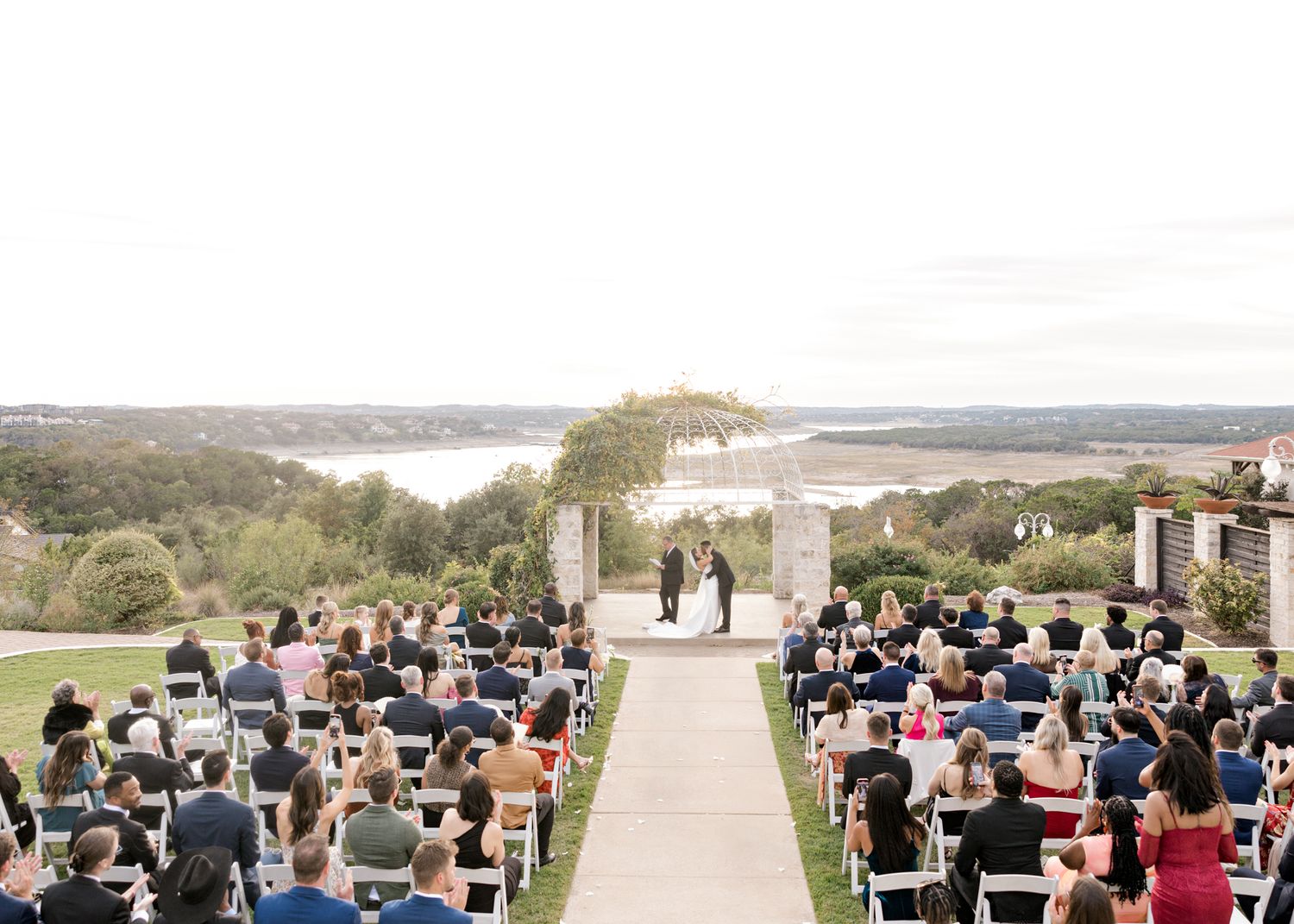 An outdoor wedding ceremony with guests seated overlooking a picturesque lake view.
