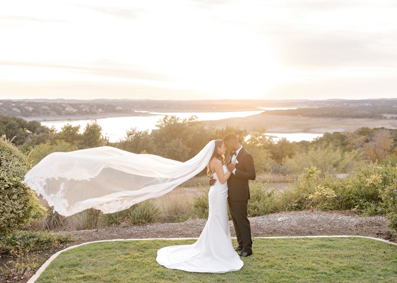 A bride's veil flows dramatically in the wind during sunset portraits on a hilltop.