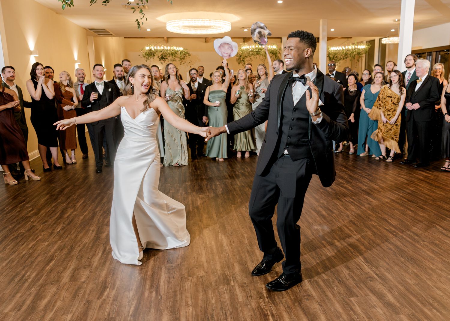 Wedding couple performs energetic dance moves during reception while guests cheer.