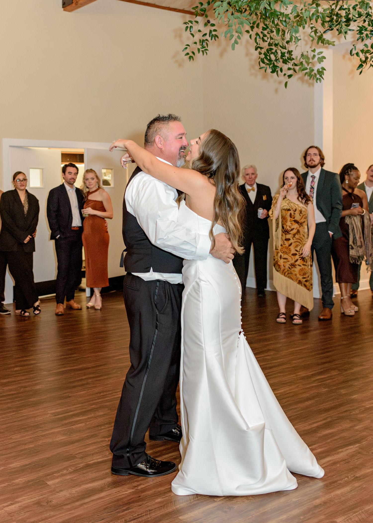 Dancing couple embraces on wooden dance floor during wedding reception.