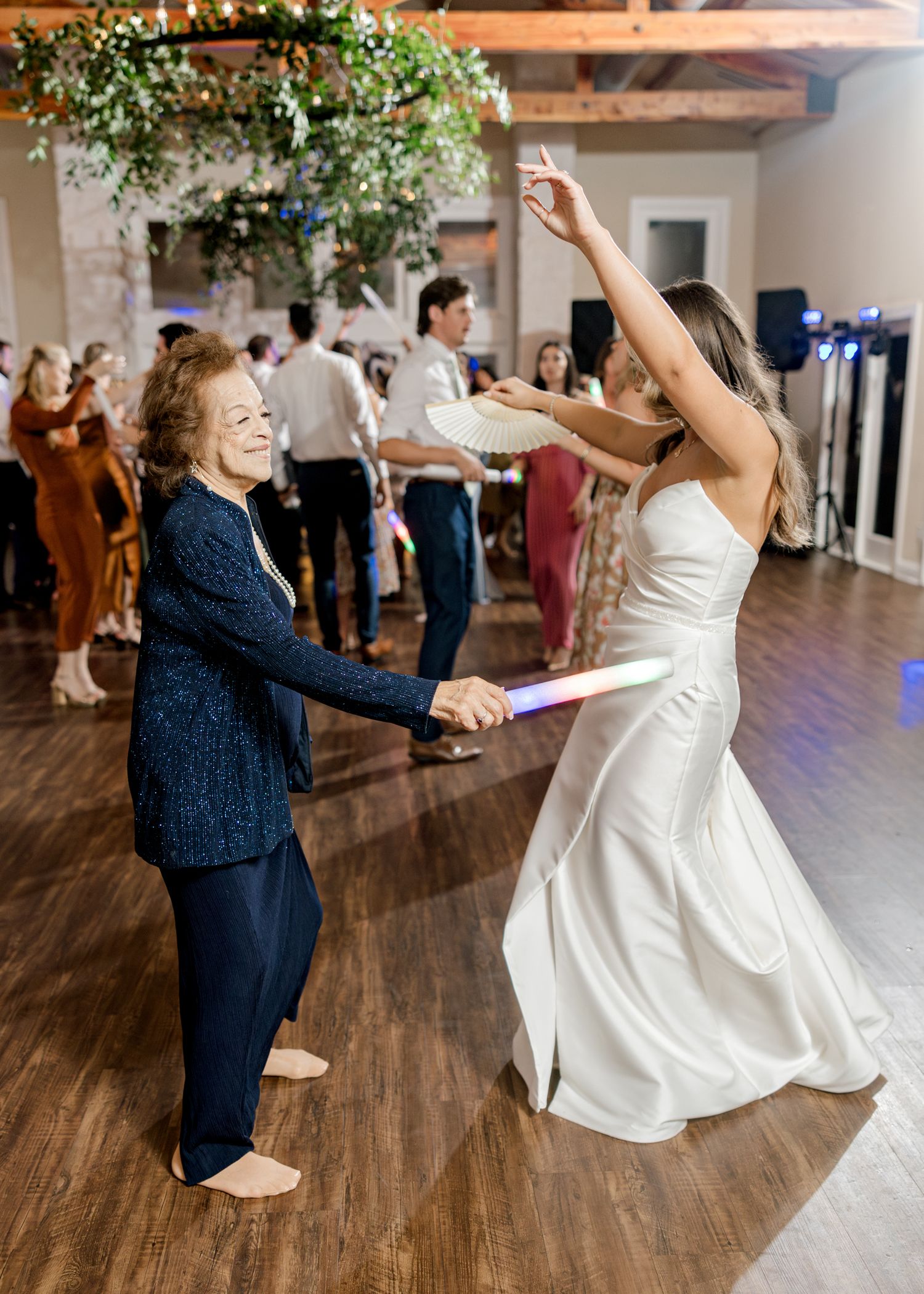 Wedding attendees dancing with enthusiasm under decorative greenery chandeliers in an indoor venue.