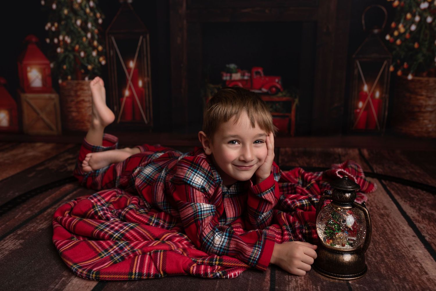 Child in red plaid pajamas sits on wooden floor with vintage phone during Christmas holiday photoshoot.