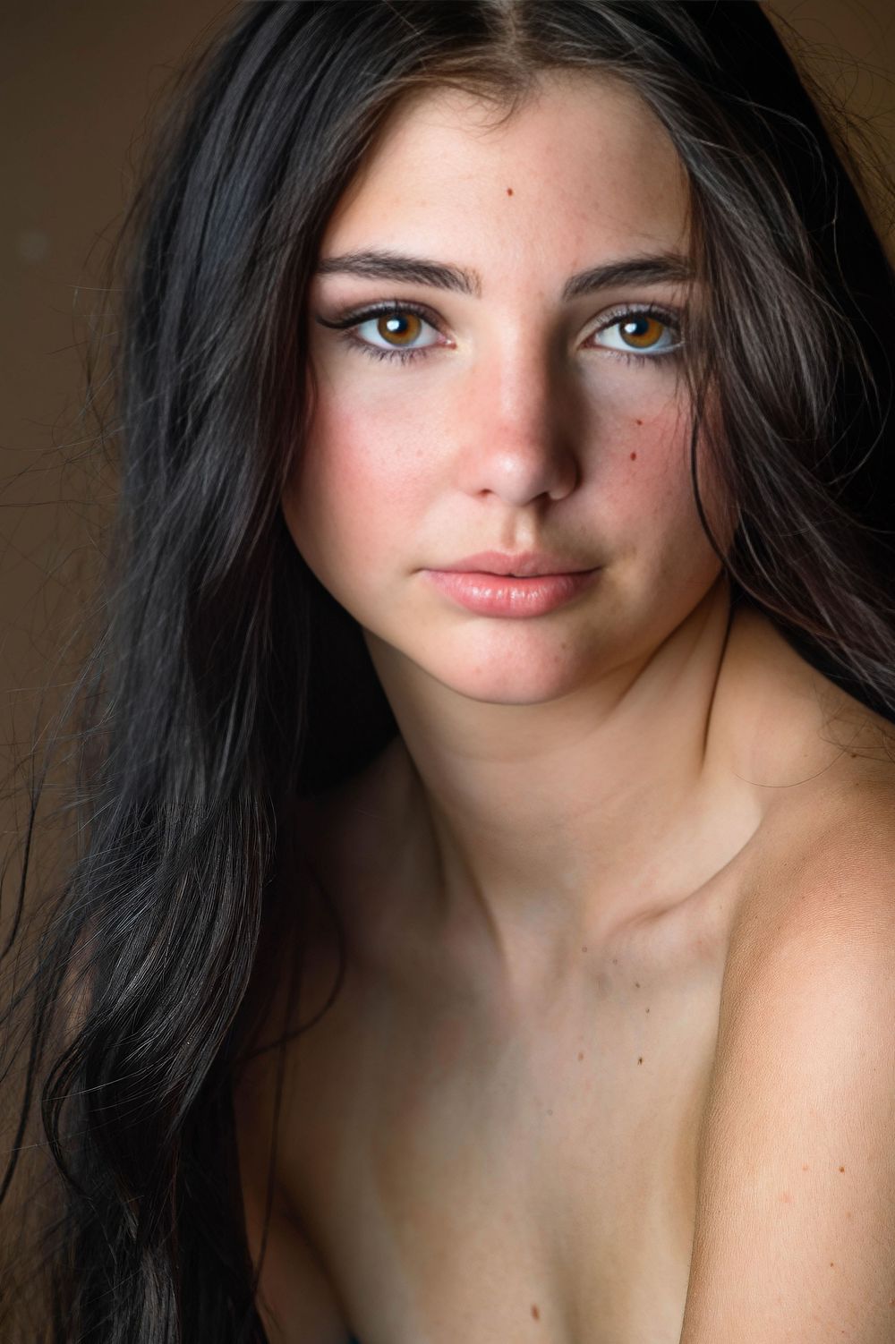A stunning portrait photo of a person with dark hair and natural makeup looking off-camera in soft lighting.