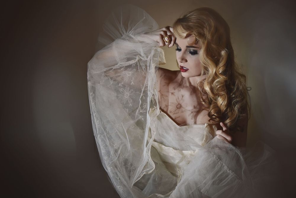 Dramatic portrait featuring flowing white tulle fabric and vintage-inspired styling in moody lighting.